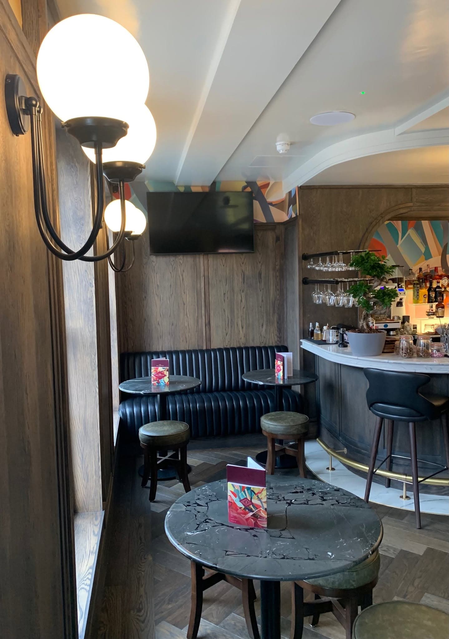 Leather banquette seating against timber wall panelling, with globe wall lights and round tables.