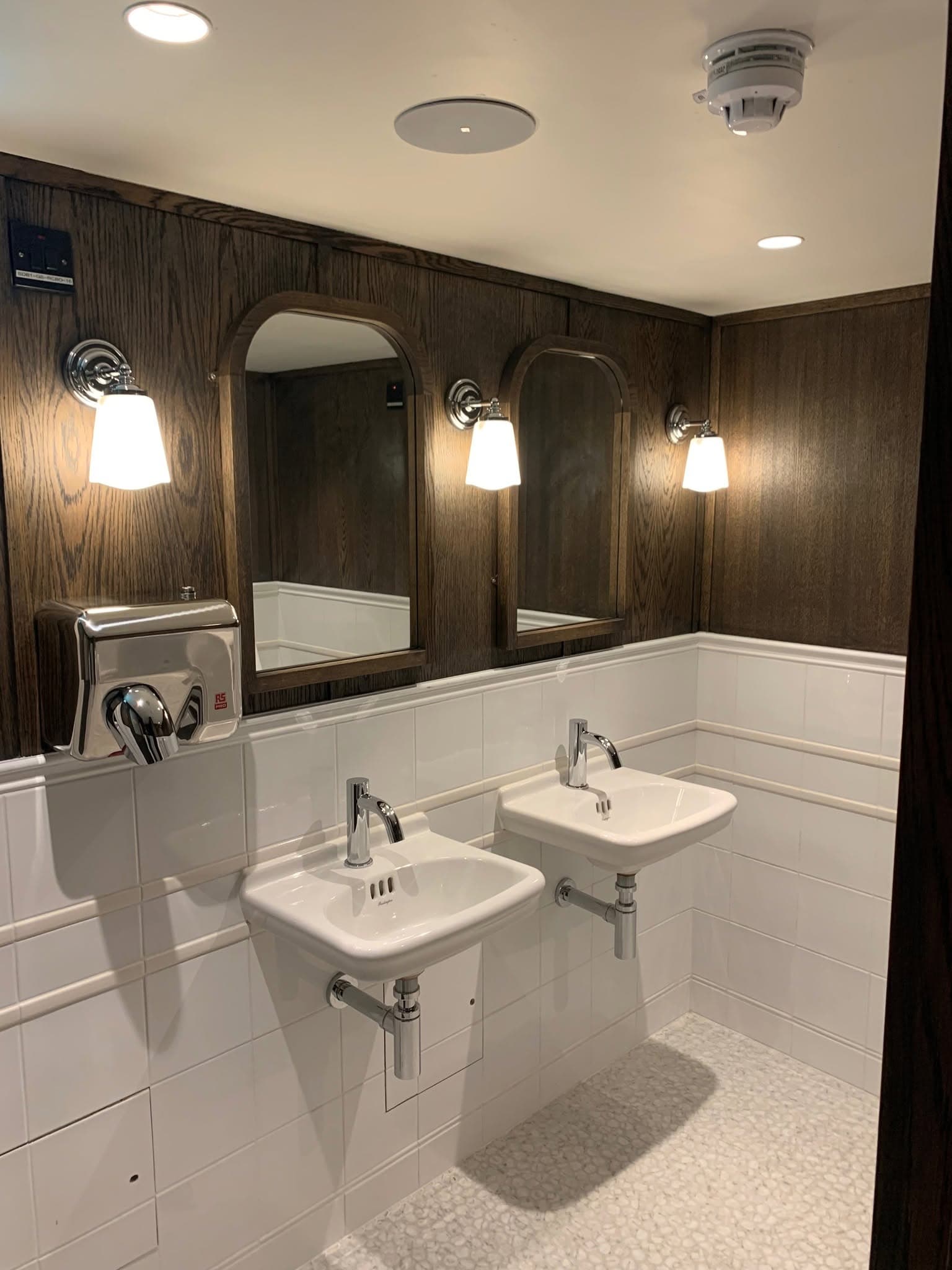 Washrooms finished in dark timber panelling and white wall tiling, with arched mirrors and twin basins.